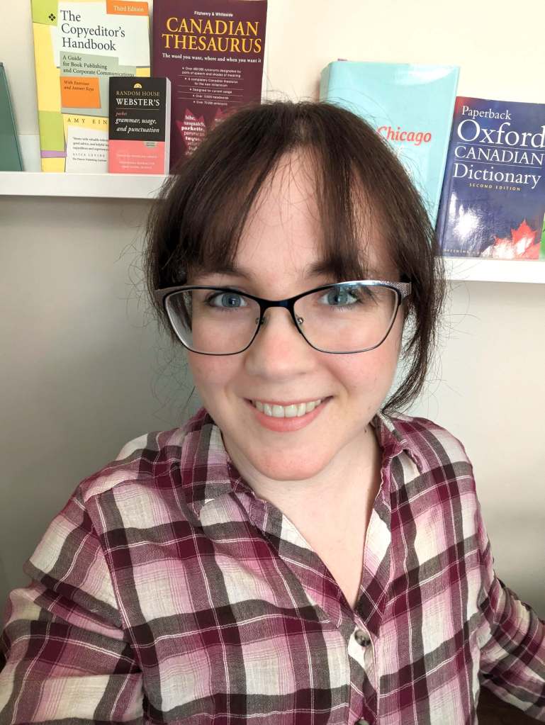 Erin, a white woman in her thirties with brown hair and large glasses, wearing a collared plaid shirt, sits in front of a shelf holding several dictionaries, thesauruses, and style guides.
