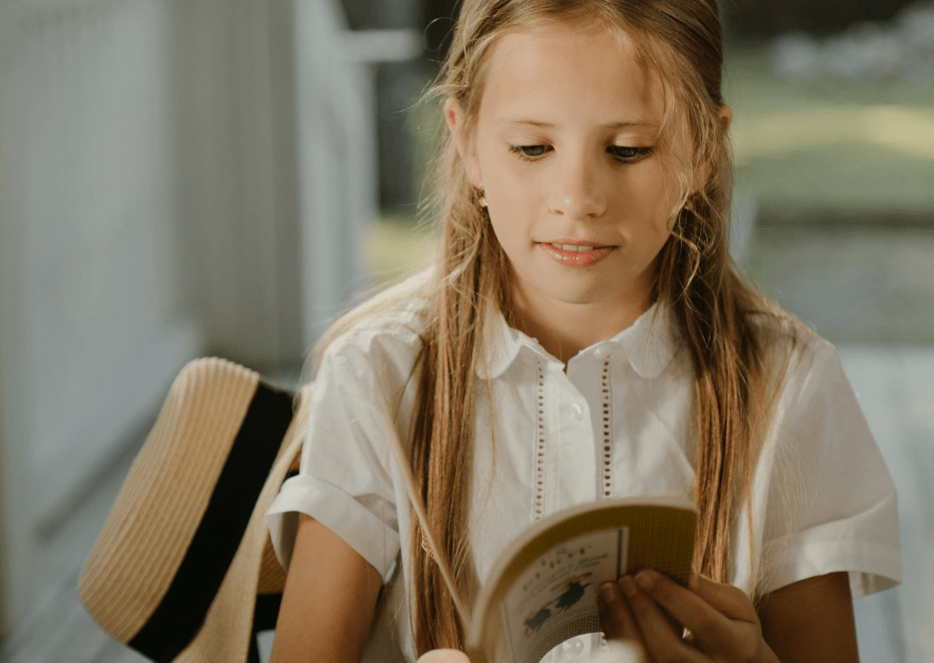 A girl reads a thin chapter book with a rabbit on the cover.