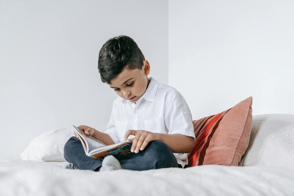 A small boy attentively reads a thin chapter book with a colourful cover. 